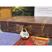 Közelkép egy dekoratív, lakattal lezárt fadobozt imitáló játékelemről a Crimes & Capers: Lady Leona’s Last Wishes társasjátékból, karakterfüzetekkel a háttérben.