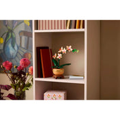 LEGO Mini Orchidea (10343) készlet elegánsan elhelyezve egy polcon, könyvek és dísztárgyak mellett, dekoratív elemként.