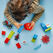 Kép egy kisgyermekről, aki a LEGO DUPLO 10424-es készlet darabjaival játszik, köztük a motorral, a Spin figurával, a piros hálóval és egy Spidey-fejet ábrázoló építőelemmel.