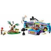 A LEGO Friends Híradós furgon (41749) járműve kinyitott állapotban, betekintést engedve a szerkesztőségi belső térbe, képernyőkkel, íróasztallal és számítógéppel. Mellette az erdei jelenet, kamerák és szereplők társaságában.