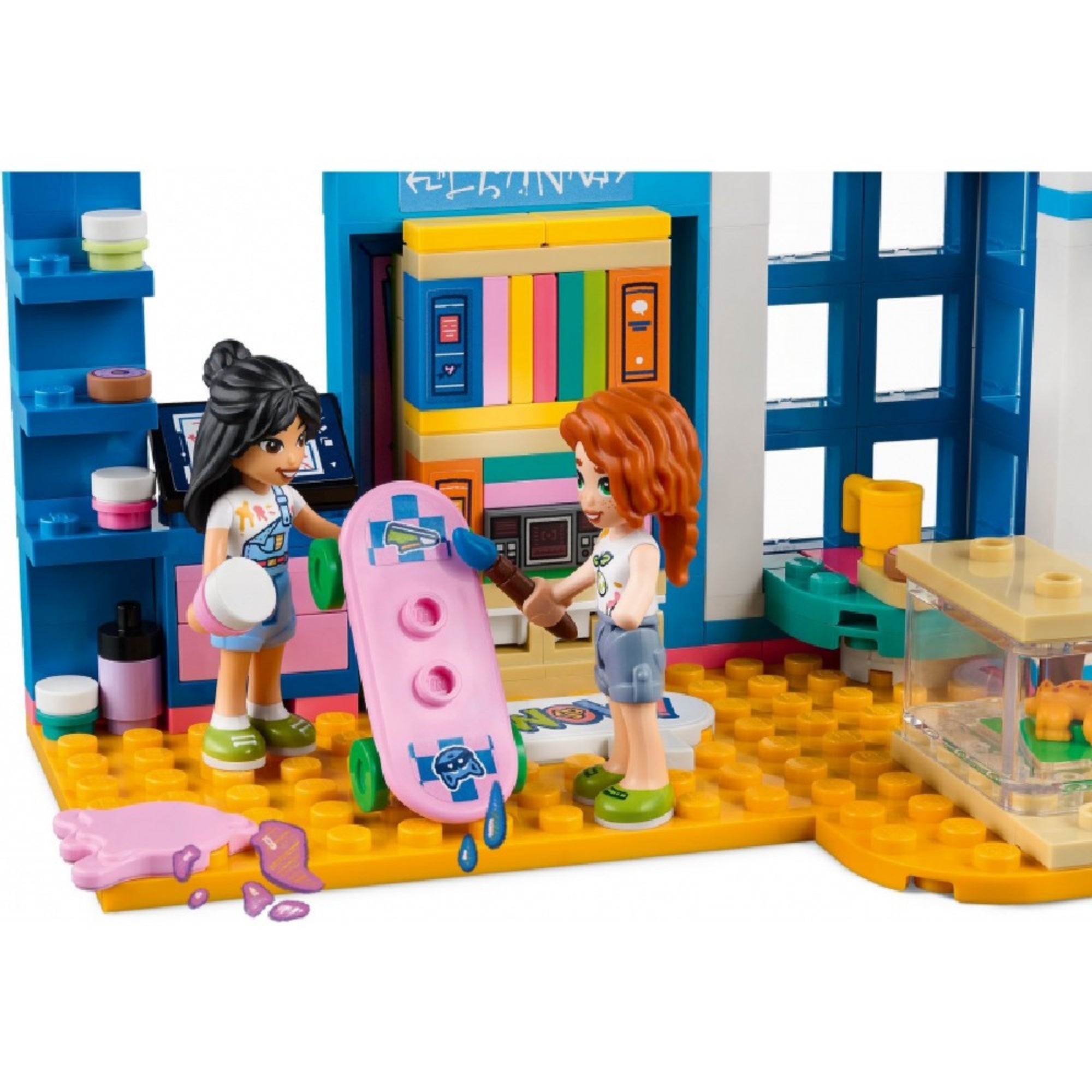 LEGO Friends 41739 Liann szobája – kreatív jelenet, amelyben a két minifigura egy rózsaszín gördeszkát dekorál ecsettel és festékkel. A háttérben színes szekrény, festékes flakonok és padlófólia látható. A szett kreatív alkotáshoz és szerepjátékhoz egyaránt kiváló.