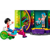 LEGO Friends 41708 Roller Disco – három minifigura találkozása a szett bejáratánál. Jackson kerekesszékben érkezik, Andrea lila táskával integet, míg Evelyn a forgóajtó mögött köszönti őket, kezében zenés és játékos kiegészítőkkel. A háttérben színes, áttetsző LEGO elemek díszítik az épület homlokzatát.