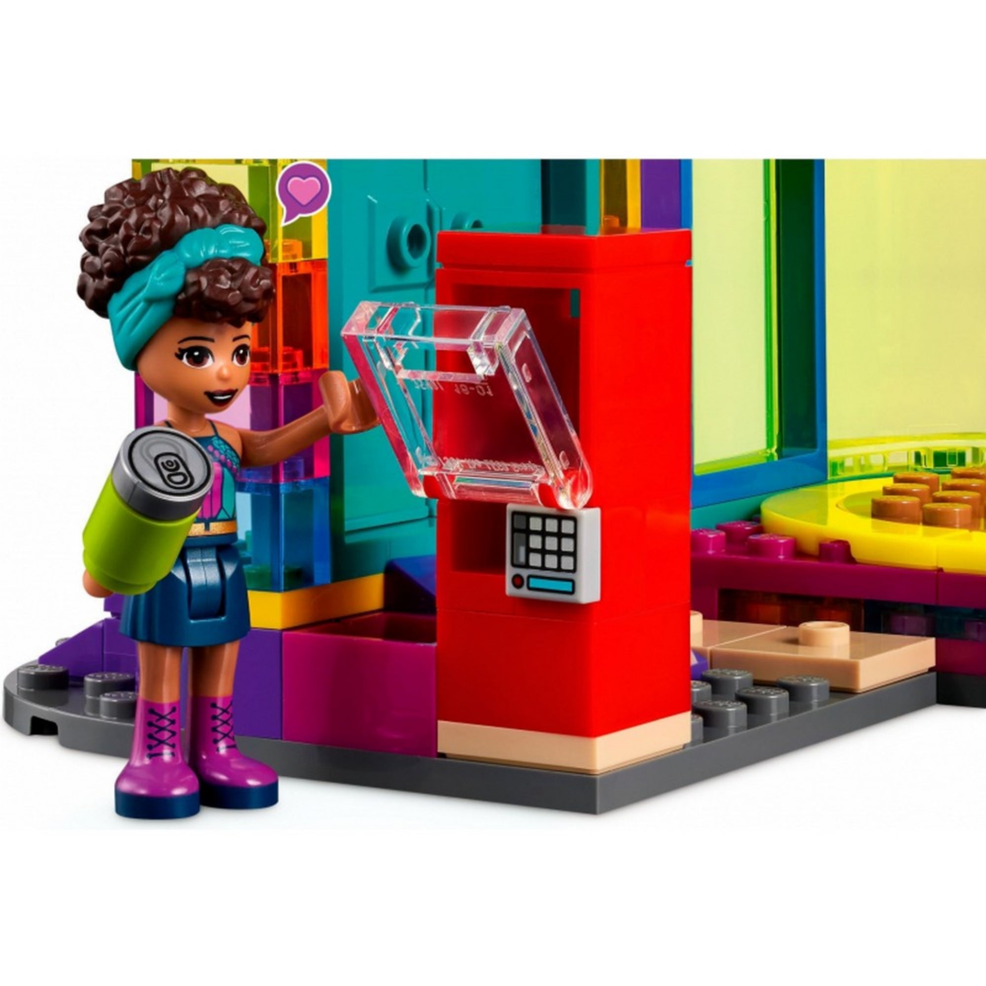 LEGO Friends 41708 Roller Disco – Andrea minifigura italautomatából vásárol zöld dobozos üdítőt. A piros automata áttetsző ajtóval és nyomógombos kezelőpanellel rendelkezik, a háttérben színes fal és táncparkett látható. A jelenet hangsúlyozza a szett interaktív játékélményét.