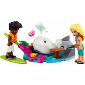 LEGO Friends 41752 Tengeri mentőrepülőgép – közelebbi jelenet, amelyben Zac evezőlapáttal, Dia pedig egy nagy villáskulccsal próbálja kiszabadítani a bálnát a sziklák közül. A víz és virágos LEGO elemek tengeri hangulatot teremtenek, miközben a bálna feje fölött egy szív alakú szökőkút jelenik meg.