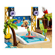 Egy szőke LEGO Friends figura szörfözik egy mozgó hullámszimulátoron, háttérben játékos tengerparti díszlet, pálmafával és hangszórókkal – LEGO Friends Tengerparti vidámpark (41737).