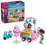 Ezen a képen a LEGO Friends Vattacukorárus stand és robogó 42643 szett látható. Az előtérben a rózsaszín vattacukorárus stand áll, kék-fehér csíkos tetővel és részletes dekorációkkal. Mellette egy kék robogó és két LEGO Friends minifigura, Liann és Jamila, akik a szerepjátékos jeleneteket teszik színesebbé. A kép középpontjában egy mosolygó, rózsaszín vattacukorfigura is helyet kapott, amely játékos elemet ad a szetthez.
