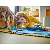 Egy gyermek játszik a LEGO City Rendőrségi motorcsónak (60456) készlettel a padlón, miközben a motorcsónak és a cápa a „vízen” úszik.