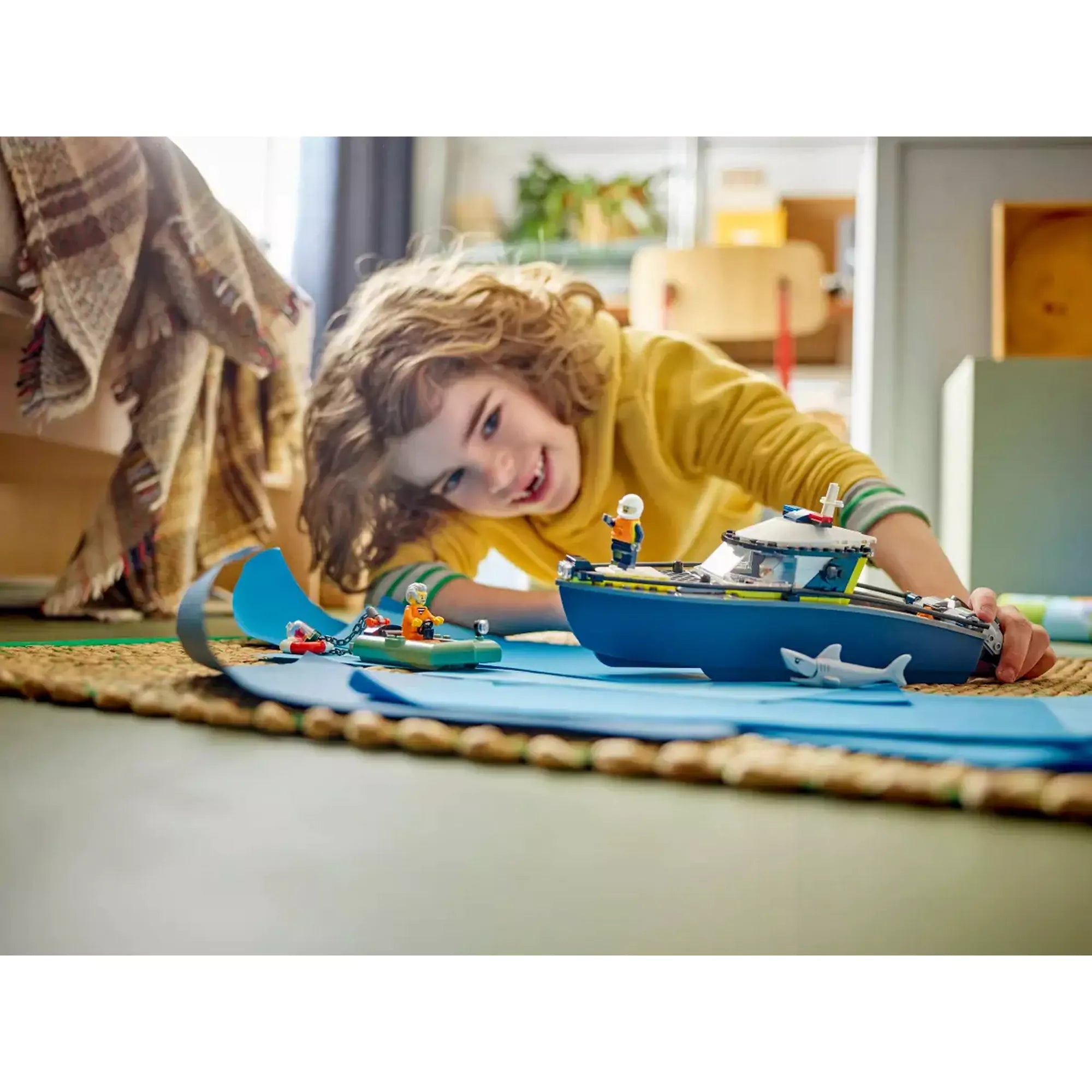Egy gyermek játszik a LEGO City Rendőrségi motorcsónak (60456) készlettel a padlón, miközben a motorcsónak és a cápa a „vízen” úszik.
