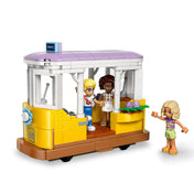 LEGO Friends: Botanikus kávéház és virágbolt (42671) sárga villamos jelenet minifigurákkal, Olly, Esma és Nova a játékos utazás közben.