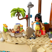 LEGO Friends 42673 jelenet, ahol egy minifigura homokba van ásva, miközben egy másik karakter lapáttal játszik a tengerparton.