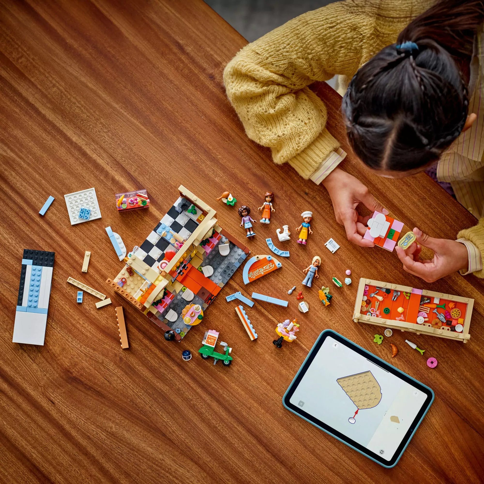 Gyerek játszik a LEGO Friends Étterem és főzőiskola 42655 építőkészlettel, miközben az építés folyamata látható.