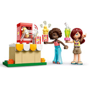 LEGO Friends – Moziest a barátokkal (42642) popcorn gép használat közben – A minifigurák egy működő popcorn gép mellett állnak, vidáman mutatják a popcornos dobozt és az üdítőt.