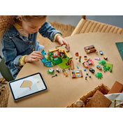 Egy gyermek épp a LEGO Friends Panda Menedékhely (42648) készletet építi, az asztalon elszórva a szett elemei, és a digitális útmutató egy tableten.
