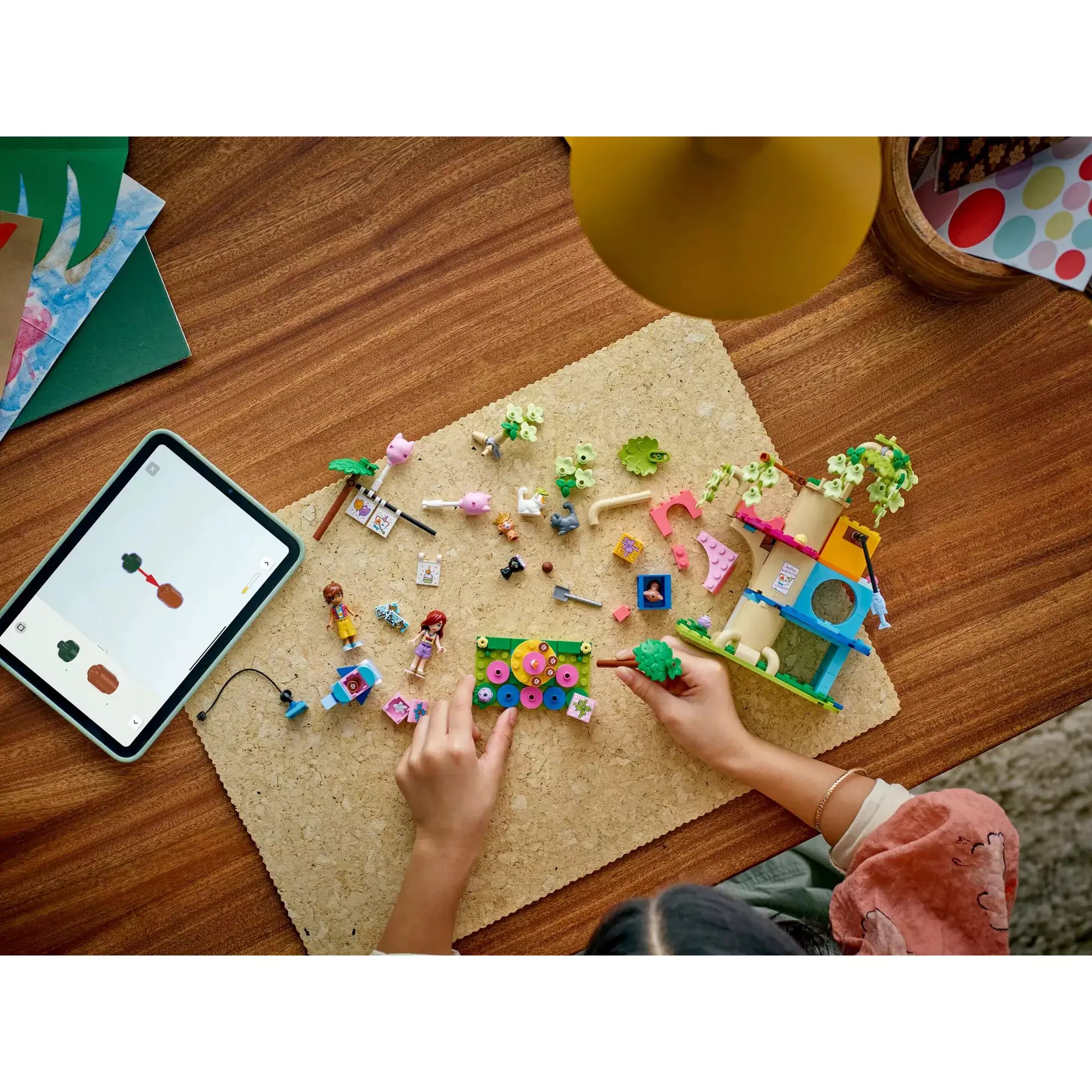 Egy gyermek építi a LEGO Friends Macskaszülinapi buli (42666) készletet asztalon, körülötte szétszórva az alkatrészek és egy tablet a digitális útmutatóval.