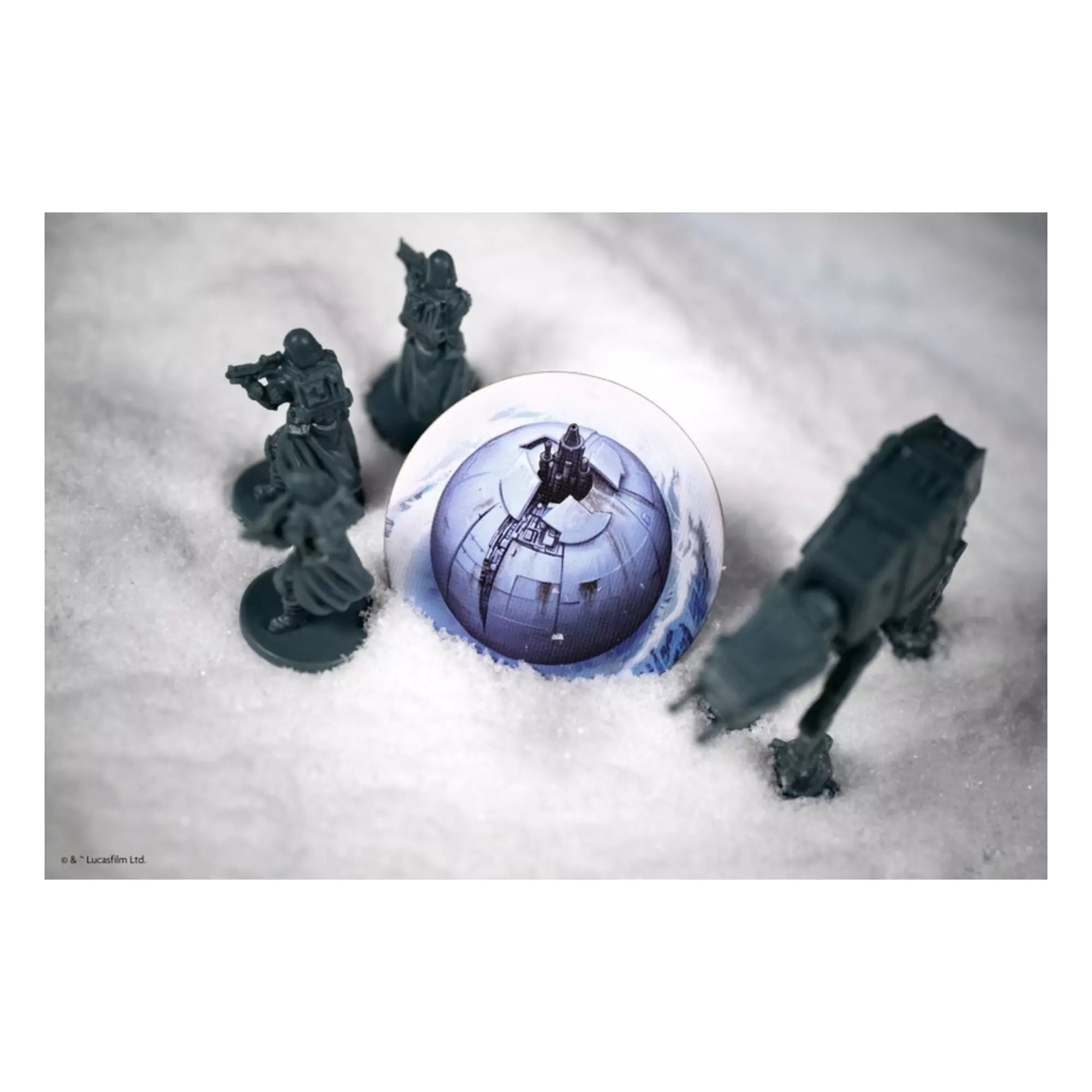 Birodalmi katonák és egy AT-AT lépegető állnak a havas terepen, egy kör alakú játékelem, a Halálcsillag illusztrációjával a középpontban.
