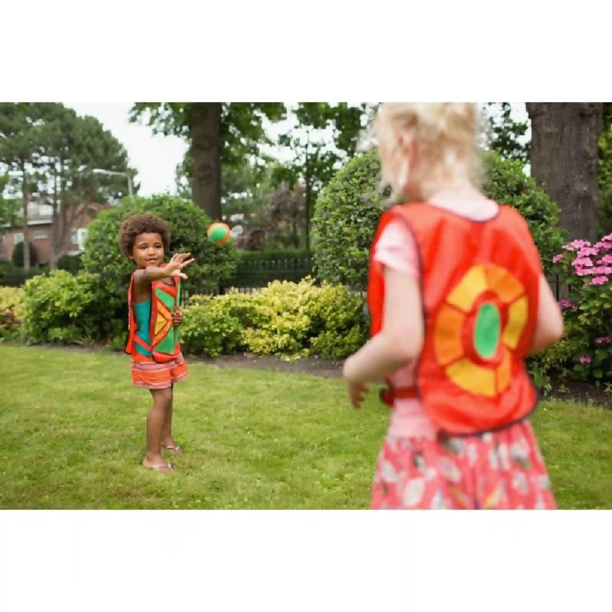 Gyerekek a BS Toys Belly Catch Set ügyességi játékkal játszanak a kertben, labdát dobva és elkapva a mellényekkel.