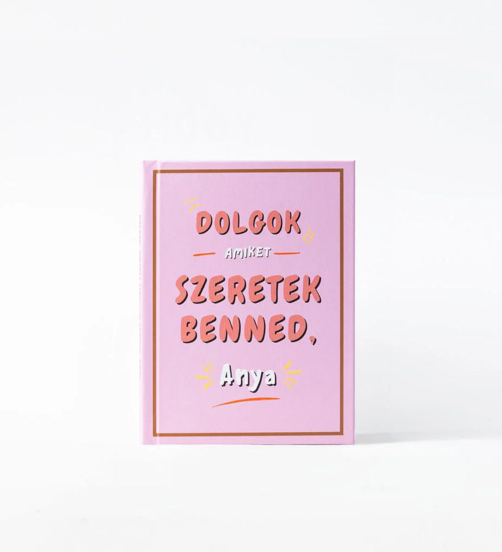 „Dolgok, amiket szeretek benned, Anya” kitölthető ajándékkönyv rózsaszín borítója, dekoratív felirattal és minimalista dizájnnal, fehér háttéren bemutatva.