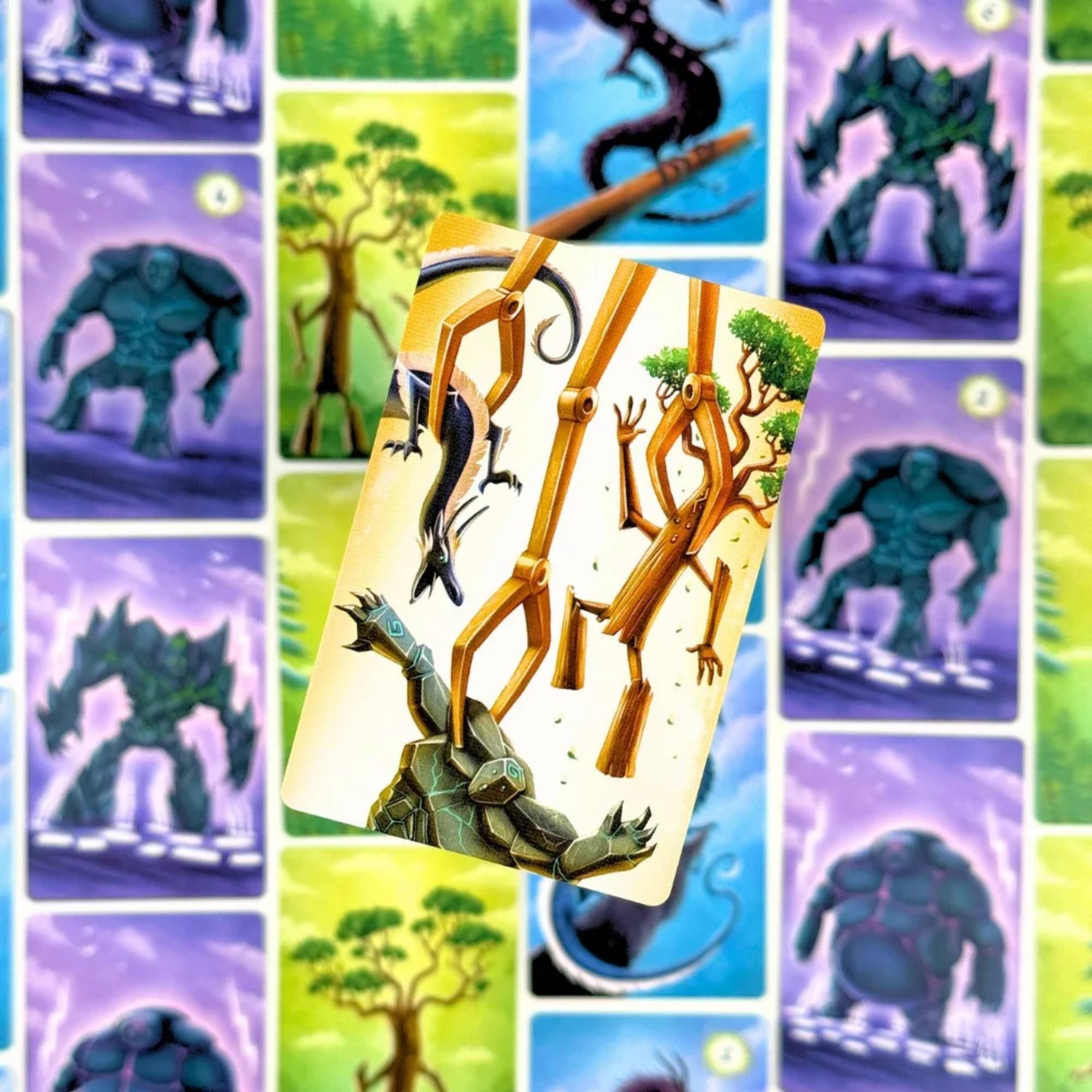 Freigard társasjáték kártya közelről, ahol egy faóriás és egy sárkányszerű lény küzd egy kőszörny ellen, színes kártyák hátterében.