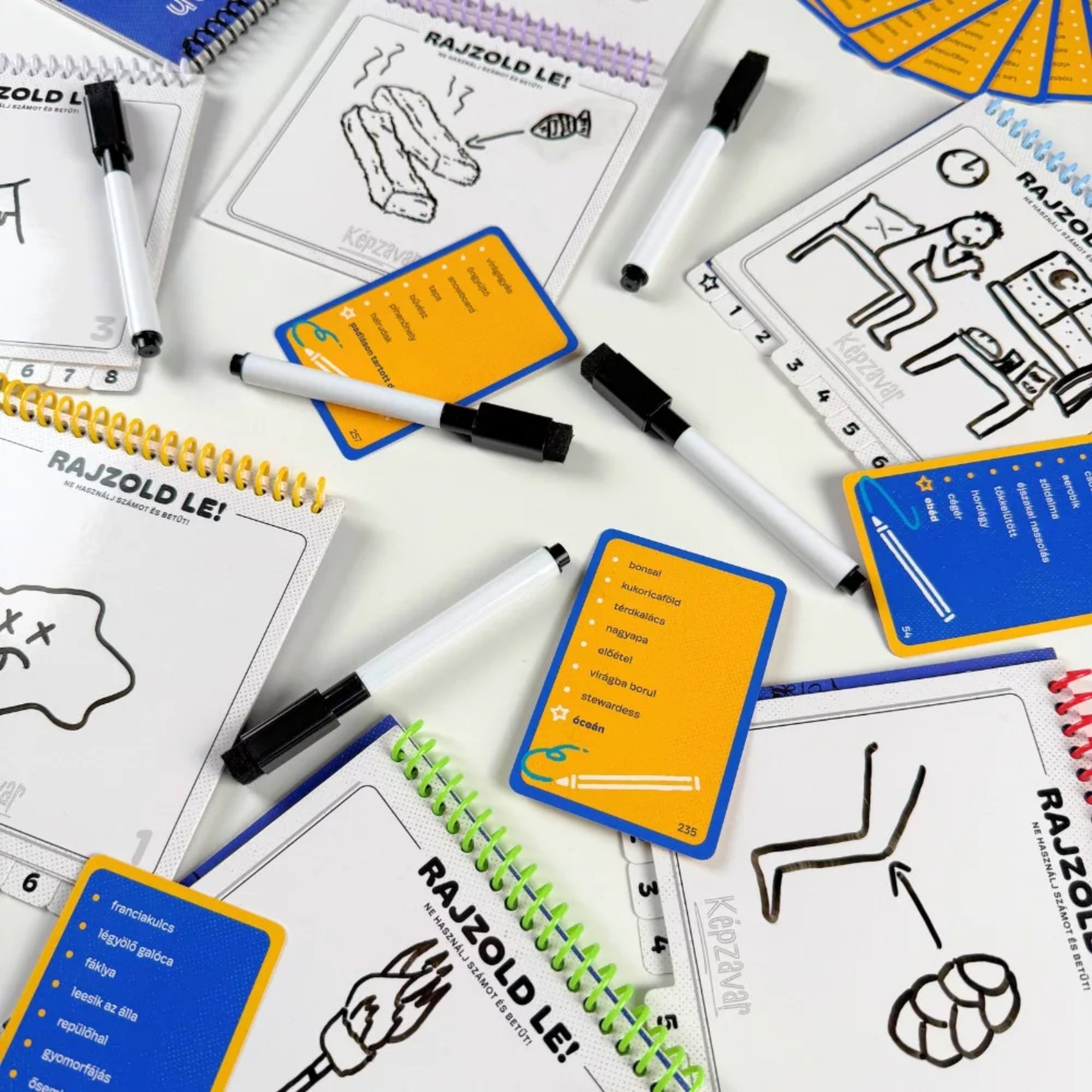Képzavar társasjáték játékmenet közben, rajzfüzetekkel, filctollakkal és feladványkártyákkal, rajzos feladatokkal az asztalon.