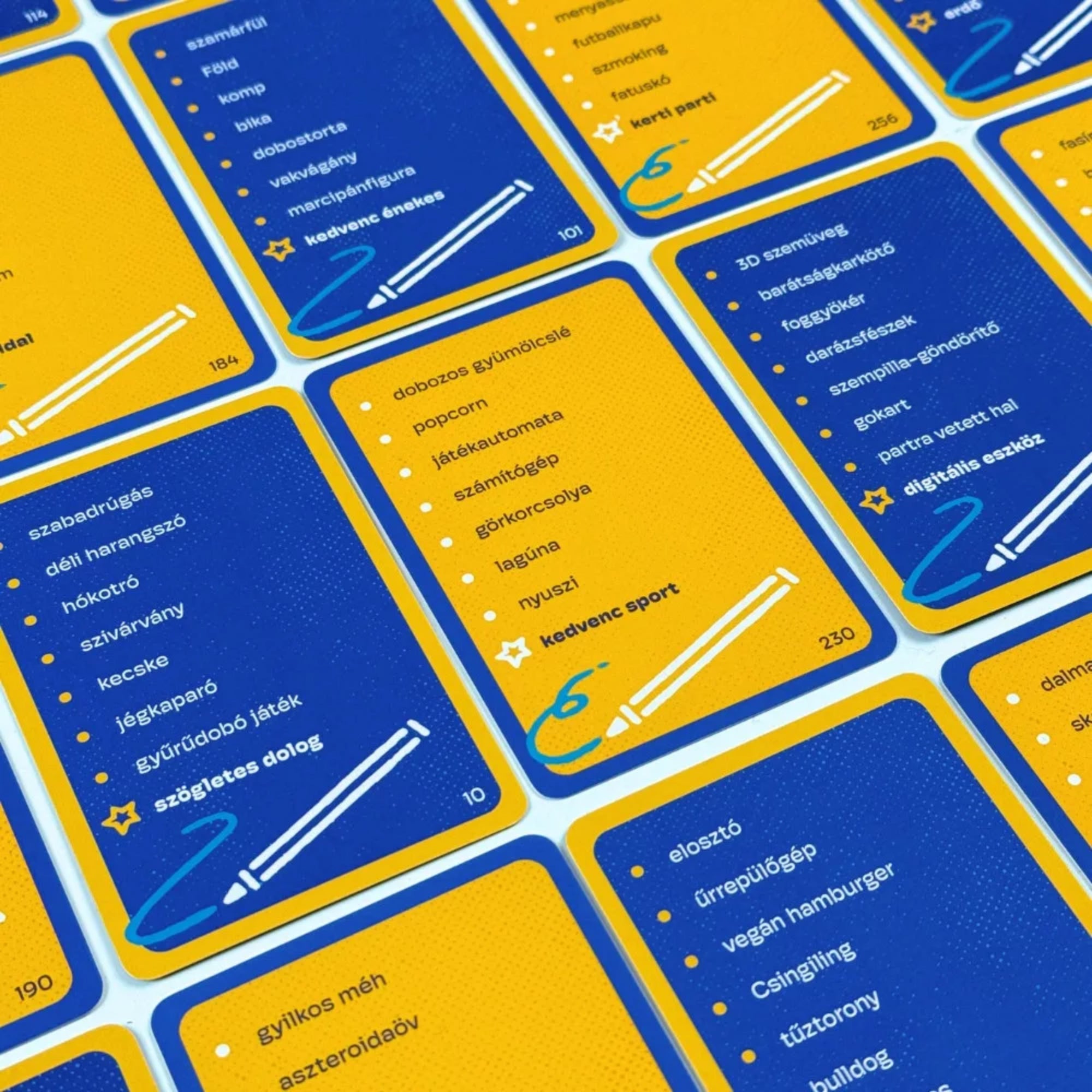 Képzavar társasjáték kártyák közelről, kék és sárga színű feladványlapokkal, rajzeszköz ikonokkal és különböző magyar szavakat tartalmazó listákkal.