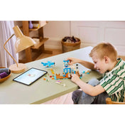 Kisfiú épp építi a LEGO Animal Crossing: Repülj a Dodo Airlines fedélzetén (77051) szettet egy asztalon, mellette tablet mutatja az útmutatót.