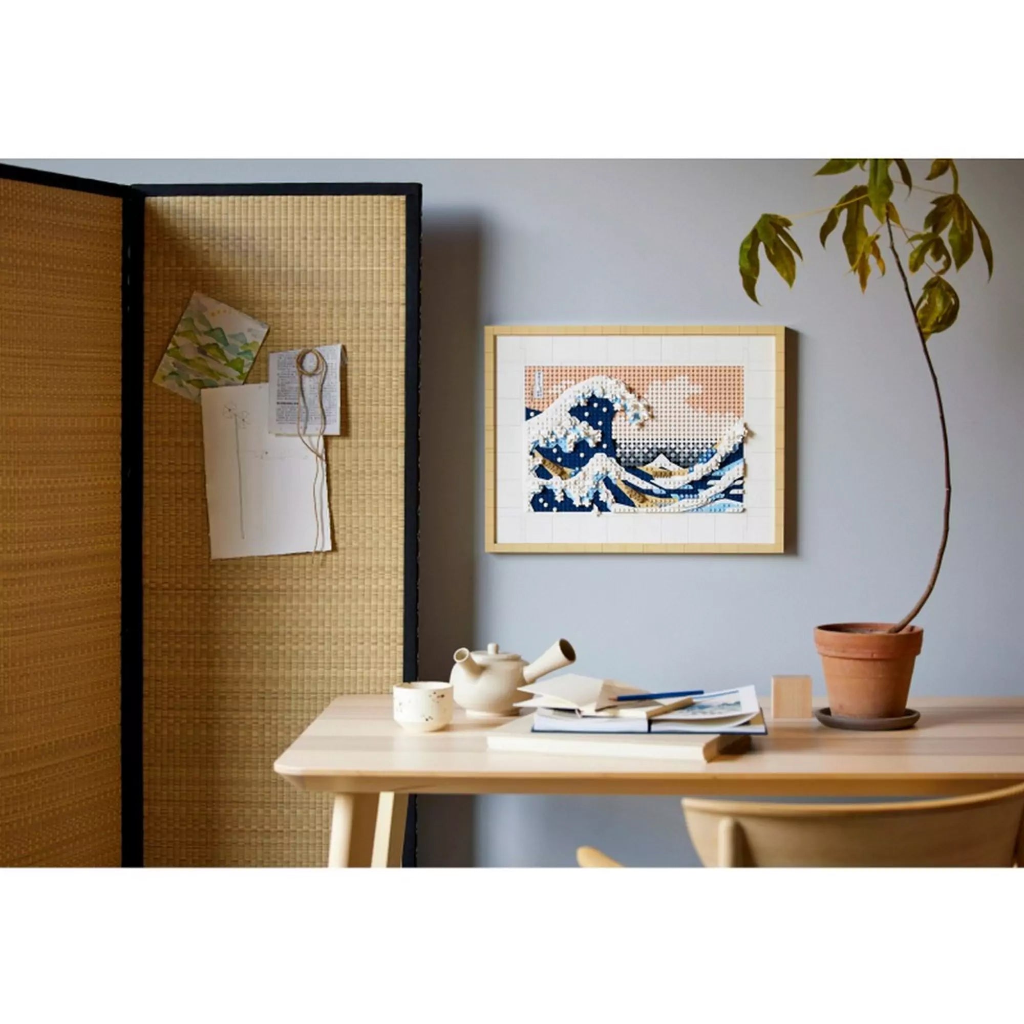 A LEGO Hokusai: A nagy hullám (31208) falra akasztott változata egy minimalista japán stílusú szobában, teáscsészékkel és könyvekkel a háttérben.