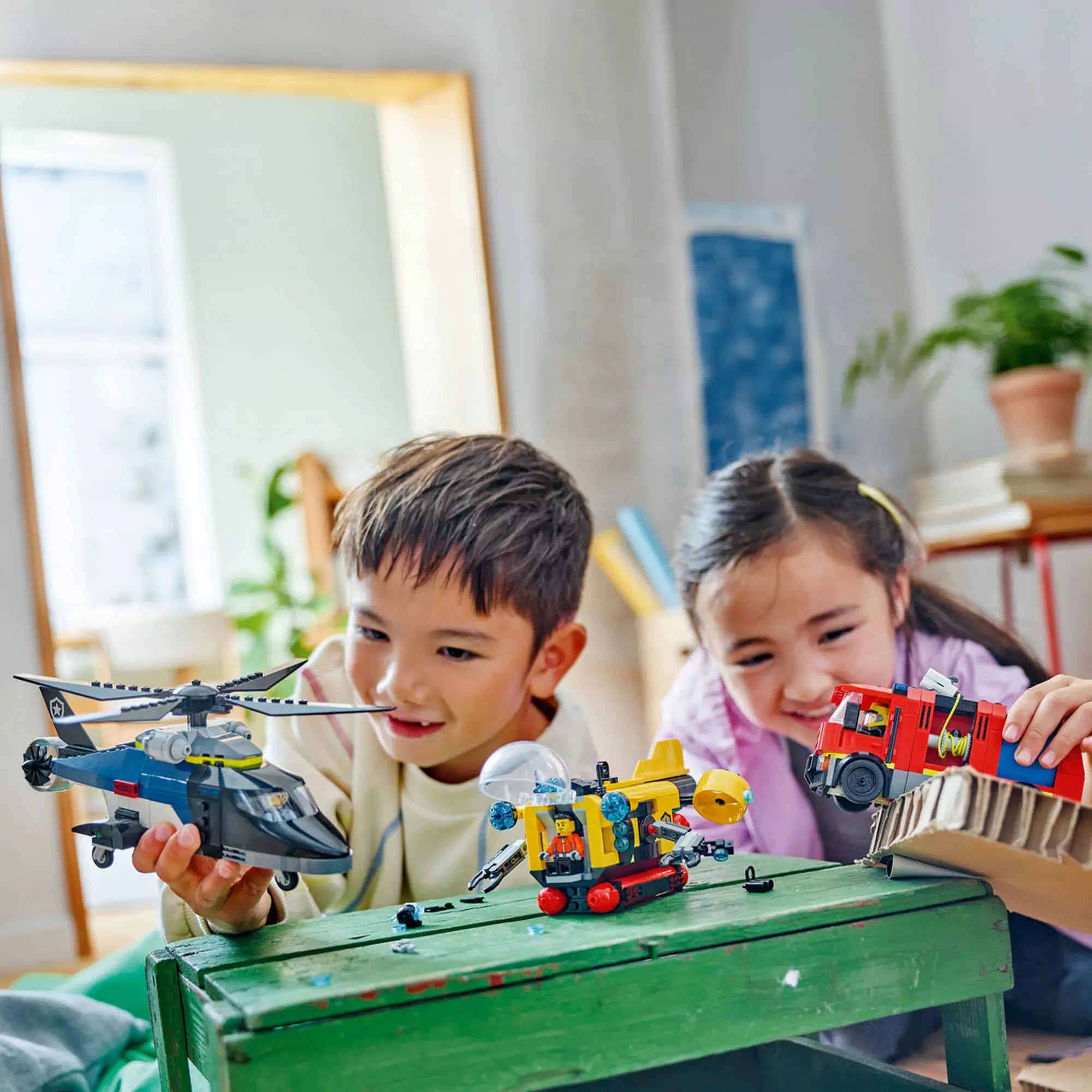 Két gyerek játszik a LEGO City Helikopter, tűzoltóautó és tengeralattjáró modellekkel.