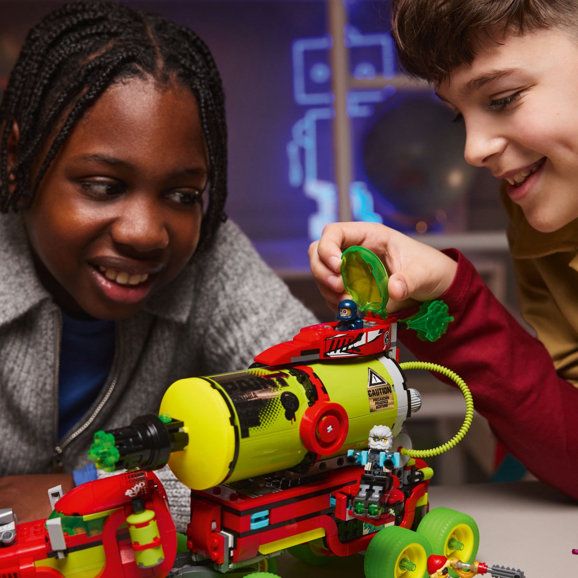Két fiú LEGO DREAMZzz Mateo festékszóró kocsijával játszik, egyikük egy figurát helyez a jármű tetején lévő nyitható zöld búrába.