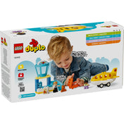 Egy kisgyermek játszik a LEGO DUPLO 10443 repülőtéri készlettel: a sárga repülőgép, torony, figurák és poggyászdarabok mellett fekszik, miközben mosolyogva tologatja a narancssárga bőröndöt.