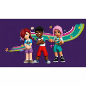 LEGO Friends Otthonos kabinok a kalandtáborban (42624) készlet három minibaba figurája lila háttér előtt. Paisley, Zac és Sky színes túraruhában láthatók, mögöttük vidám, festett szivárványos grafika és kalandtábori motívumok.