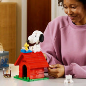 LEGO Ideas Snoopy kutyaháza (21368) életképen, ahol egy rajongó a megépített modellt állítja be, kiemelve Snoopy és Woodstock részletgazdag LEGO figuráit.