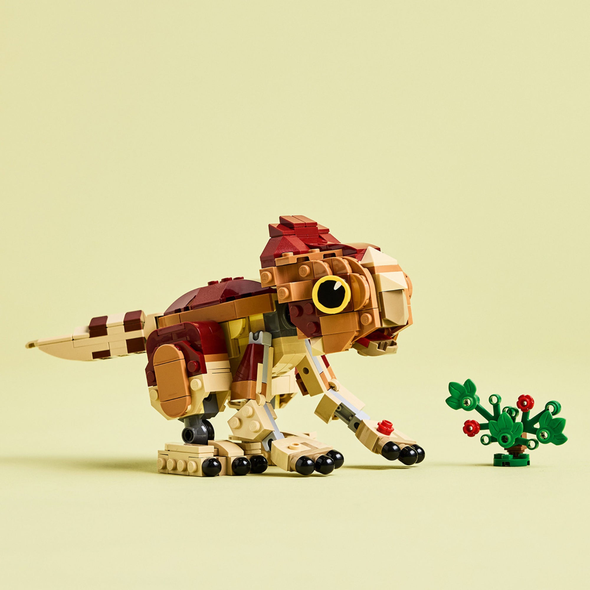A LEGO Jurassic World Baby Dinosaur Dolores: Aqiulops (76970) készlet aranyos, mozgatható dinoszaurusz figurája világos háttér előtt, zöld növénnyel.