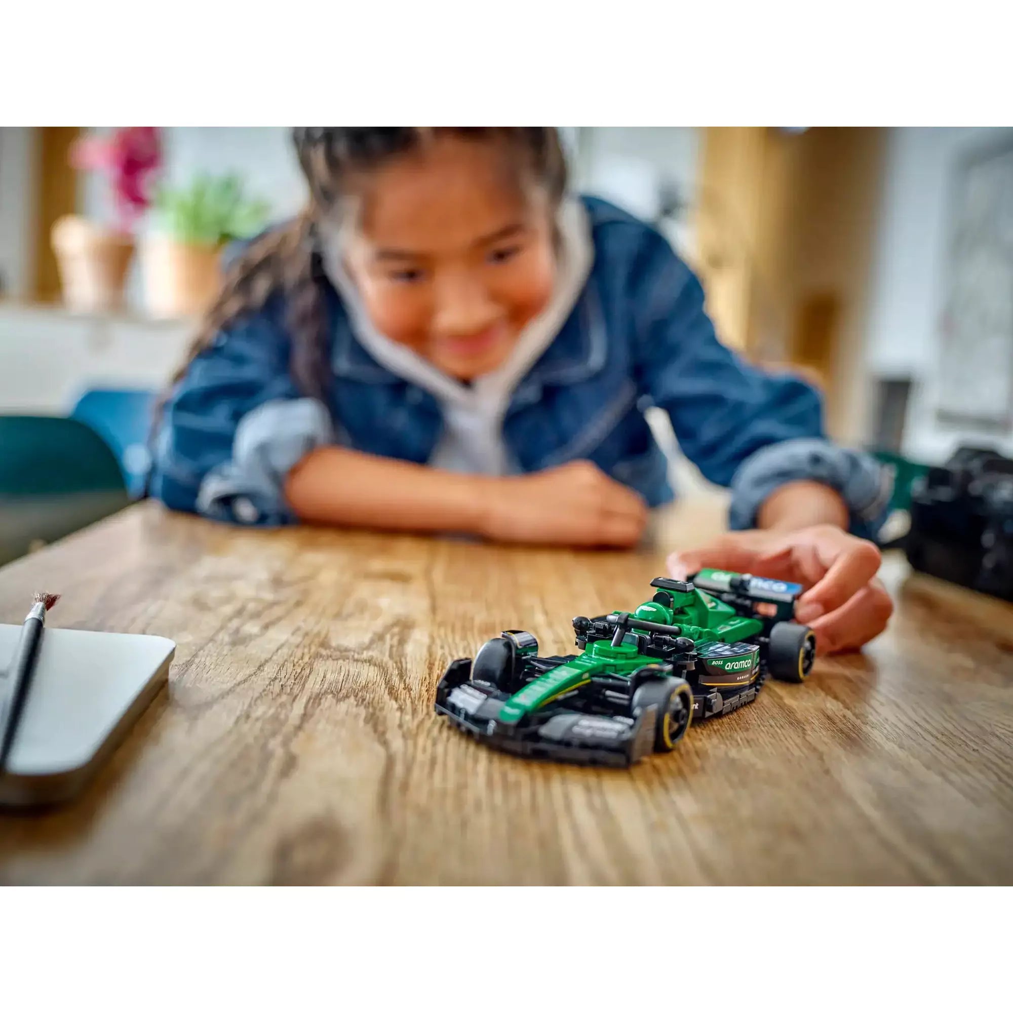 LEGO Speed Champions Aston Martin Aramco F1 AMR24 versenyautó 77245, lány játszik a versenyautóval mosolyogva.