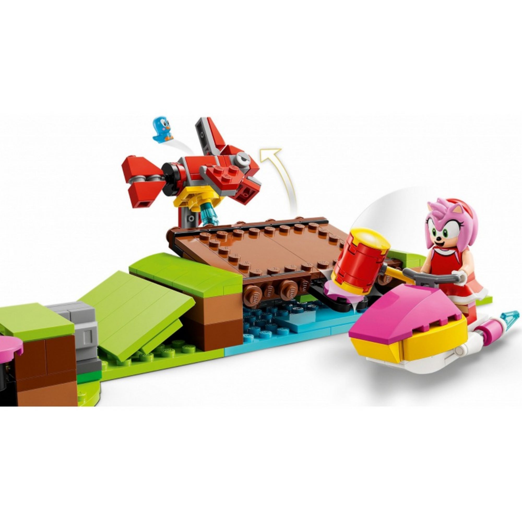 Amy rózsaszín járművén közelít egy vörös robotmadár felé a LEGO 76994-es készletből, háttérben mozgatható híd és zöld dombos elem látható.
