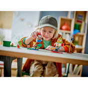 Egy kisfiú mosolyogva játszik a LEGO Super Mario 71439 készlet elemeivel, Mario a levegőben, Yoshi, Goomba és Bowser Jr. figurák a pályán elhelyezve.