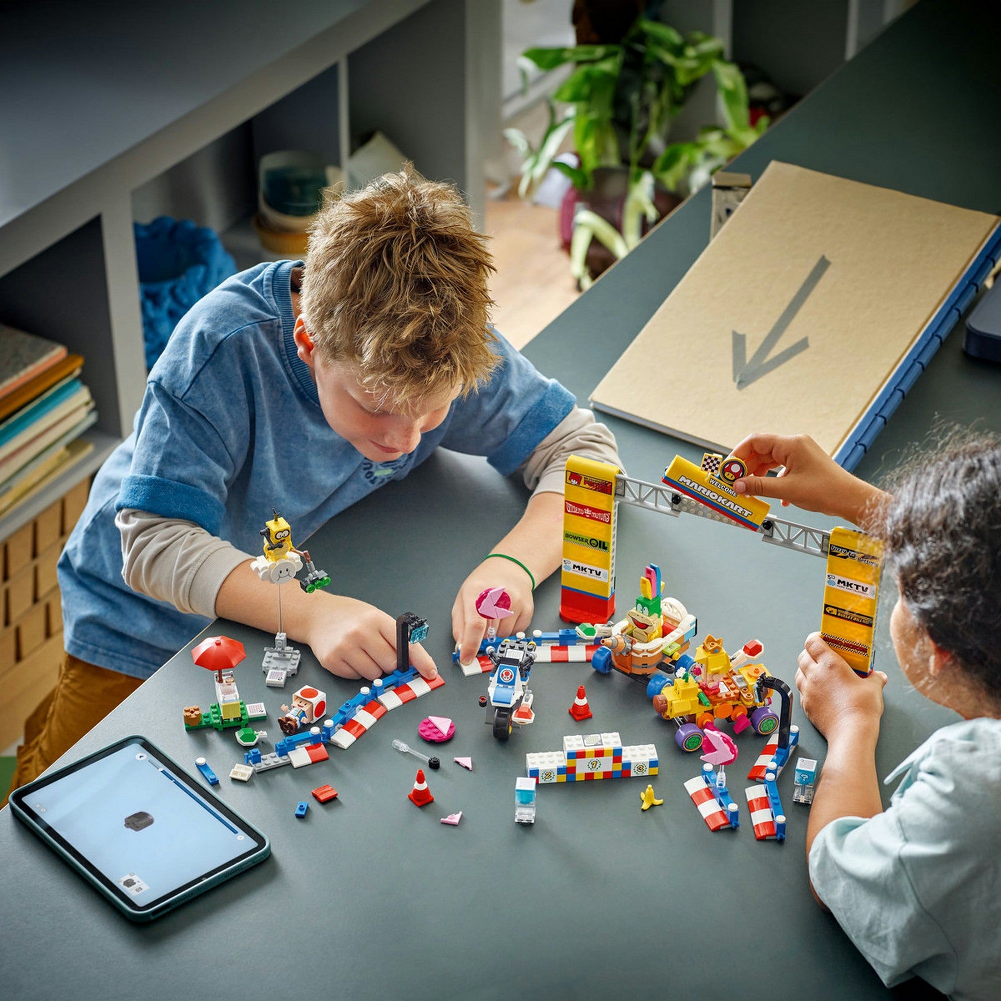 Két gyermek építi a LEGO Super Mario Mario Kart Baby Peach és Grand Prix szett (72036) pályáját egy asztalon.
