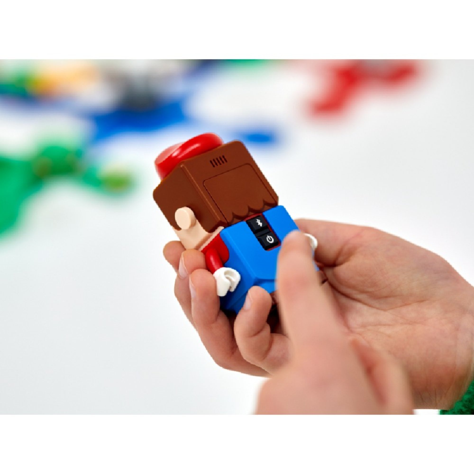 Kézben tartott LEGO Mario figura hátulnézetből, jól látszanak a bekapcsológombok és a hangszóró, amelyek az interaktív játékhoz szükségesek.