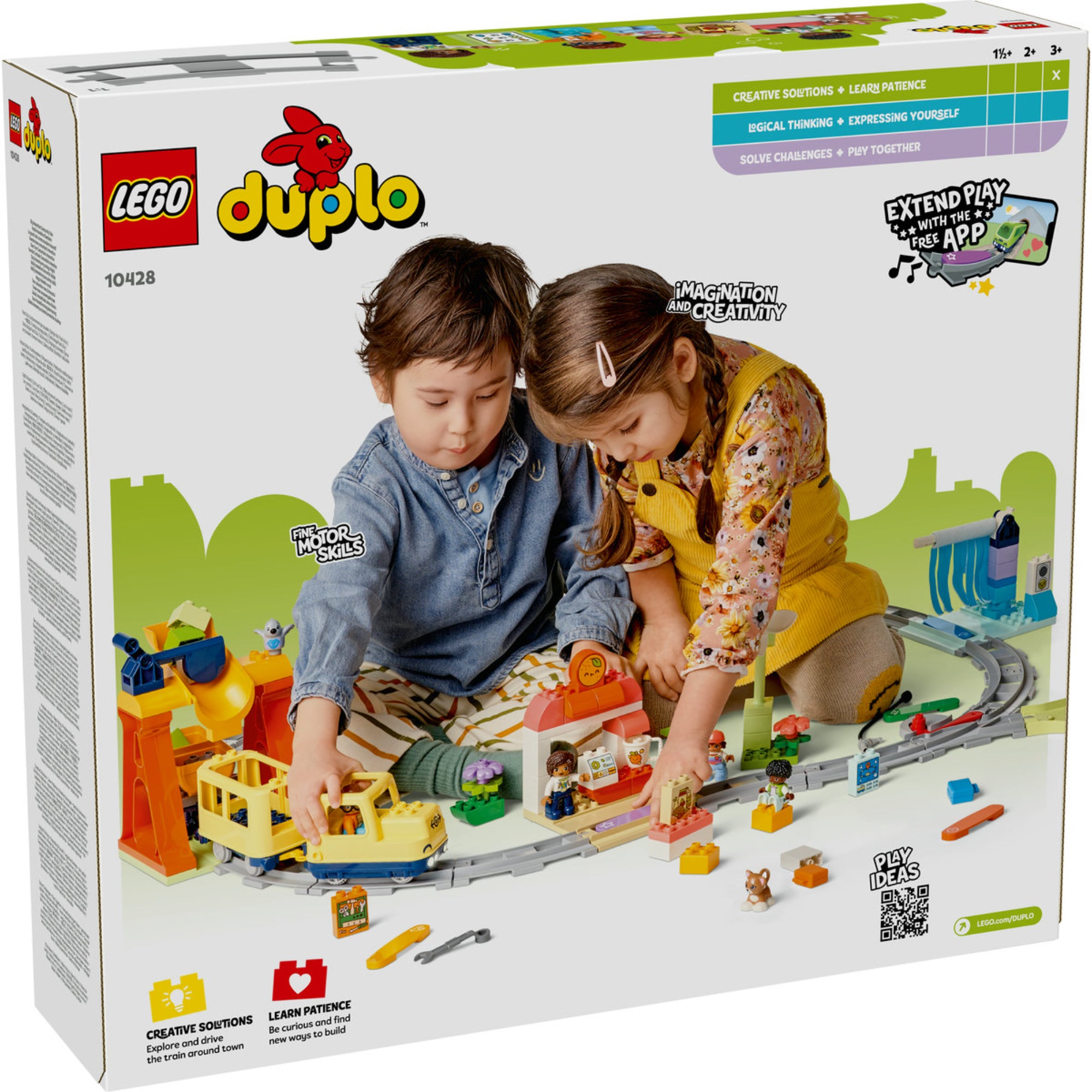 Két kisgyerek játszik a LEGO DUPLO 10428 vonatkészlettel, miközben sínpályán vezetik a sárga mozdonyt; a háttérben láthatók az állomás, akciókockák és egyéb színes építőelemek is.