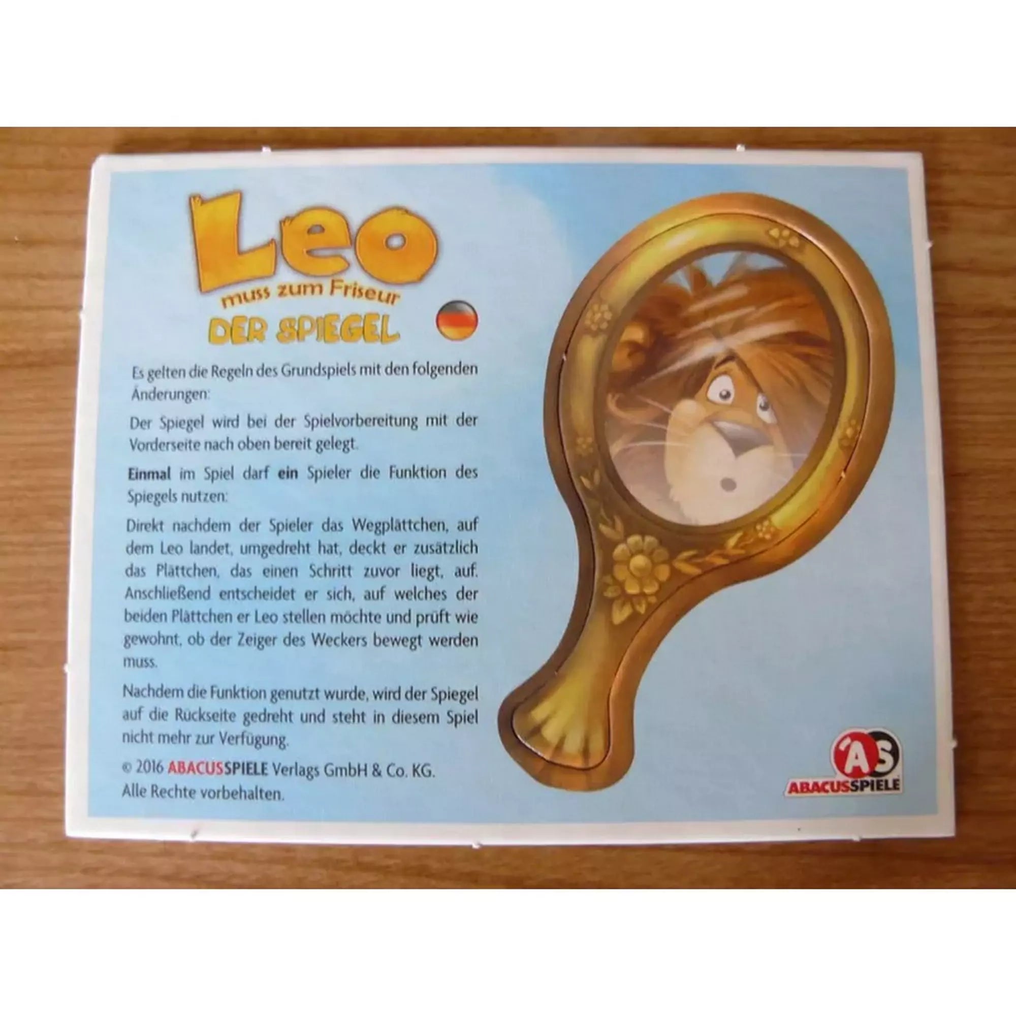 Leo – A tükör kiegészítő német nyelvű szabályleírása. A kép egy aranykeretes kézi tükröt ábrázol, amelyben Leo, az oroszlán tükörképe látható.