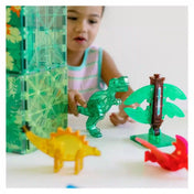 Gyermek játszik a MAGNA-TILES Dino World XL mágneses építőkészlet zöld dinoszauruszfigurájával, pálmafa és építmények mellett.
