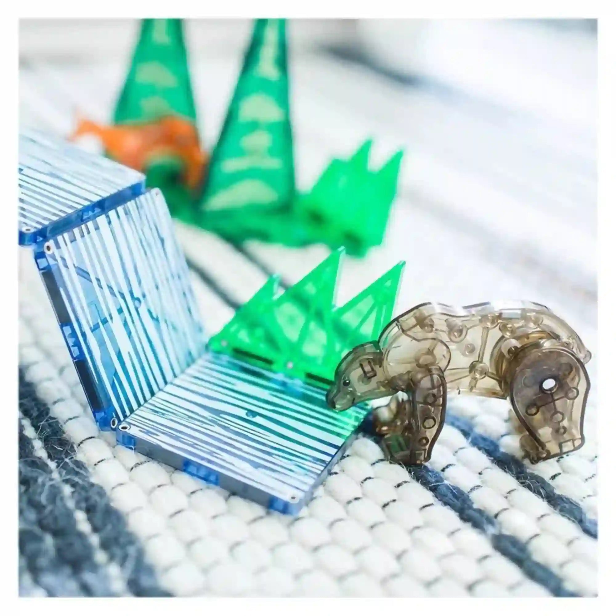 MAGNA-TILES Forest Animals mágneses építőkészlet átlátszó barna medvefigurája kék-fehér mintás mágneses lapok és zöld fenyőelemek mellett.