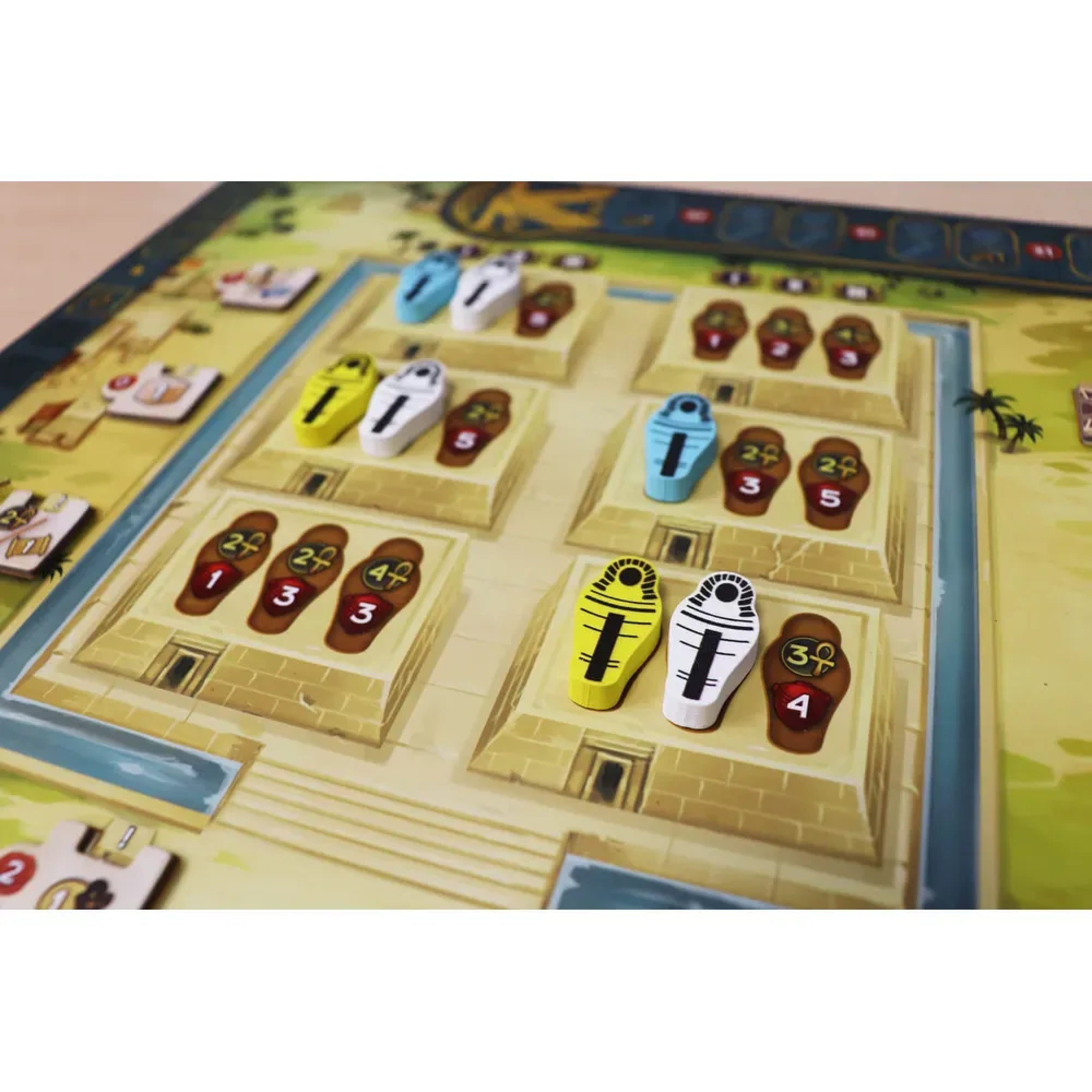 A Men Nefer társasjáték közelképe a piramisokat és szarkofágokat ábrázoló játékelemekről, különböző színű figurákkal és számértékekkel.