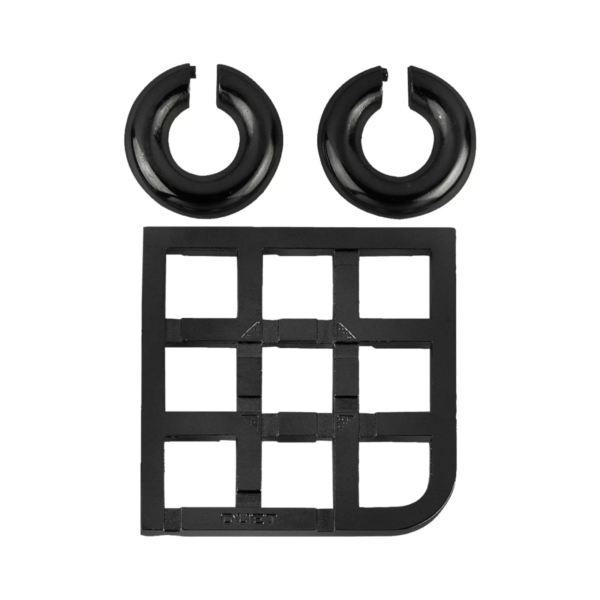 A Cast Duet puzzle darabokra szedve: két fényes fekete fémgyűrű és a négyzethálós alap külön elrendezve.