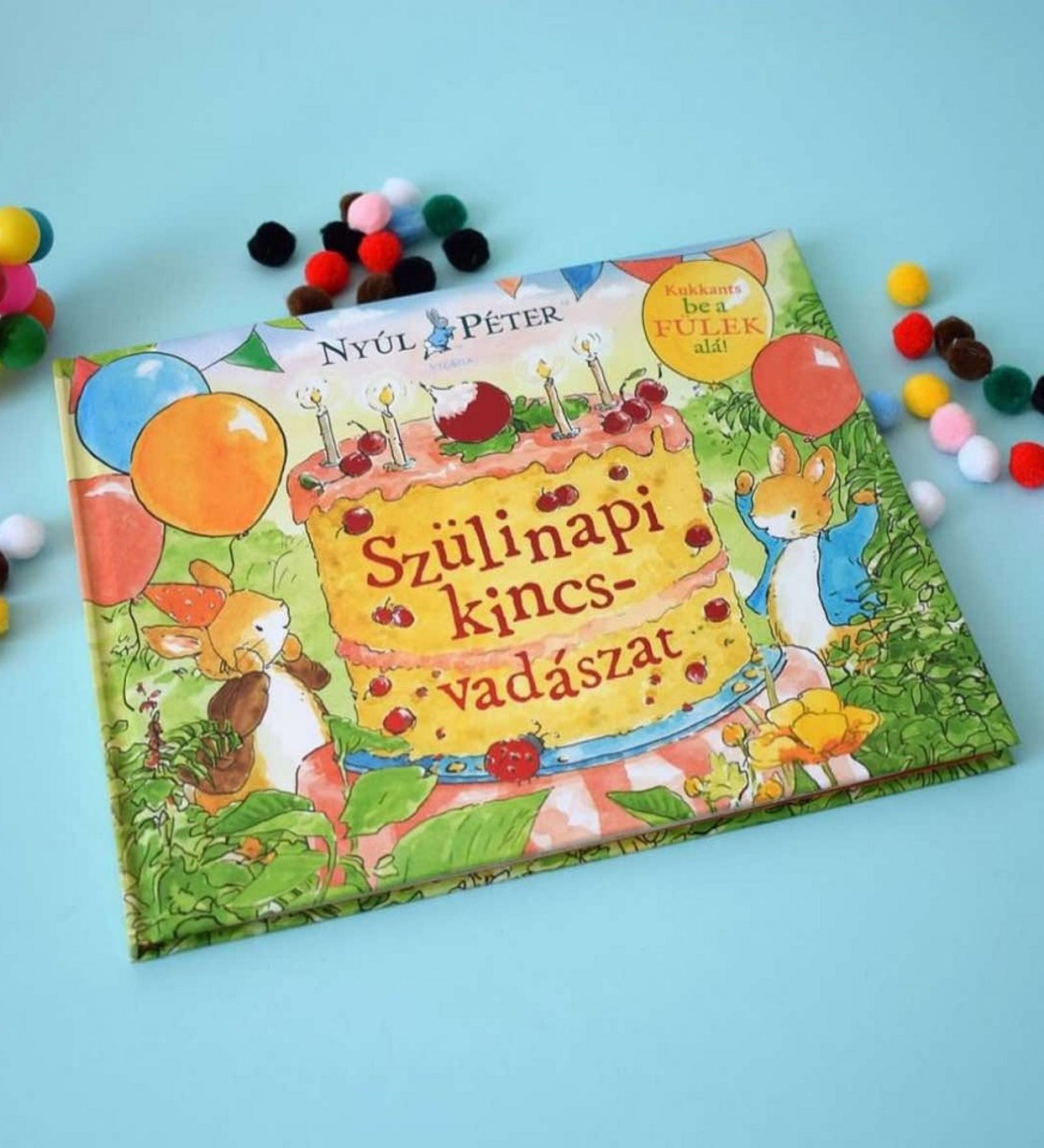 Nyúl Péter – Szülinapi kincsvadászat című mesekönyv színes borítóval, körülötte színes pomponokkal díszített háttéren.