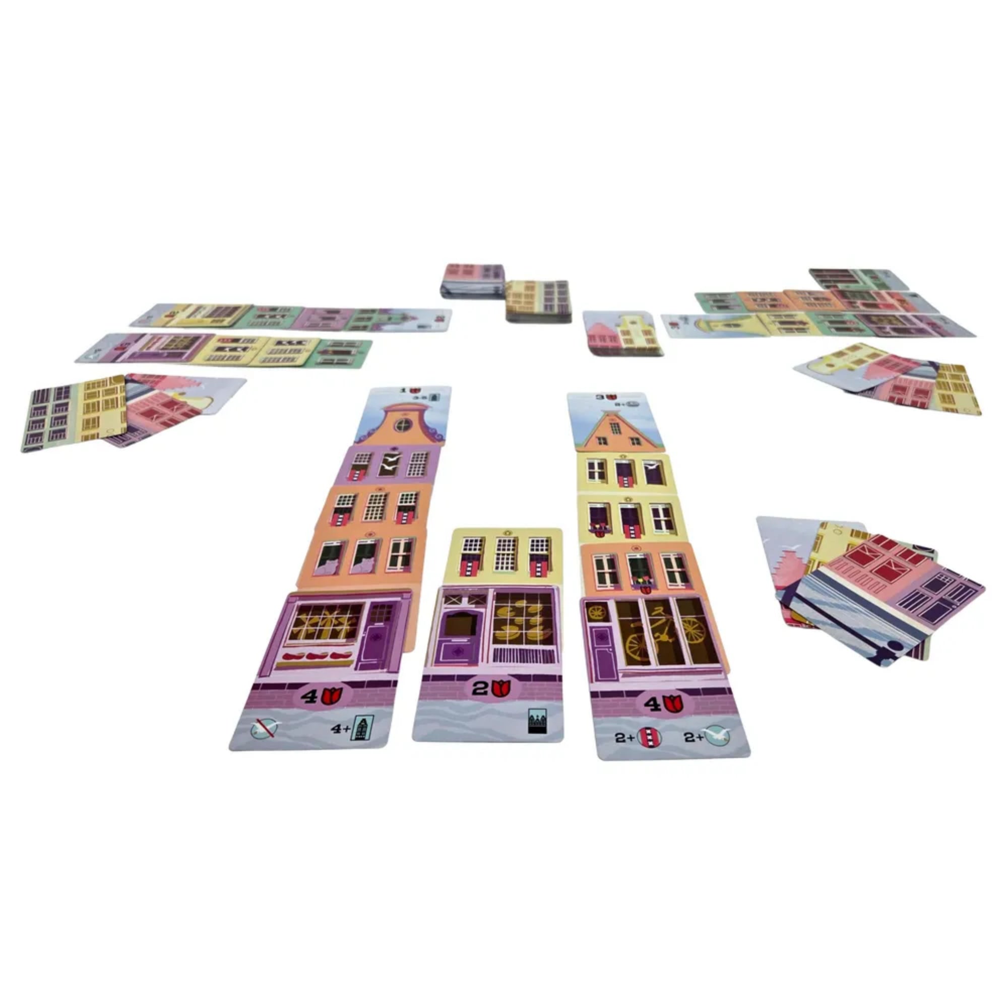  Játék közbeni elrendezés a Táncoló Házak társasjátékból, egymásra épített, színes házkártyákkal és húzópaklikkal.