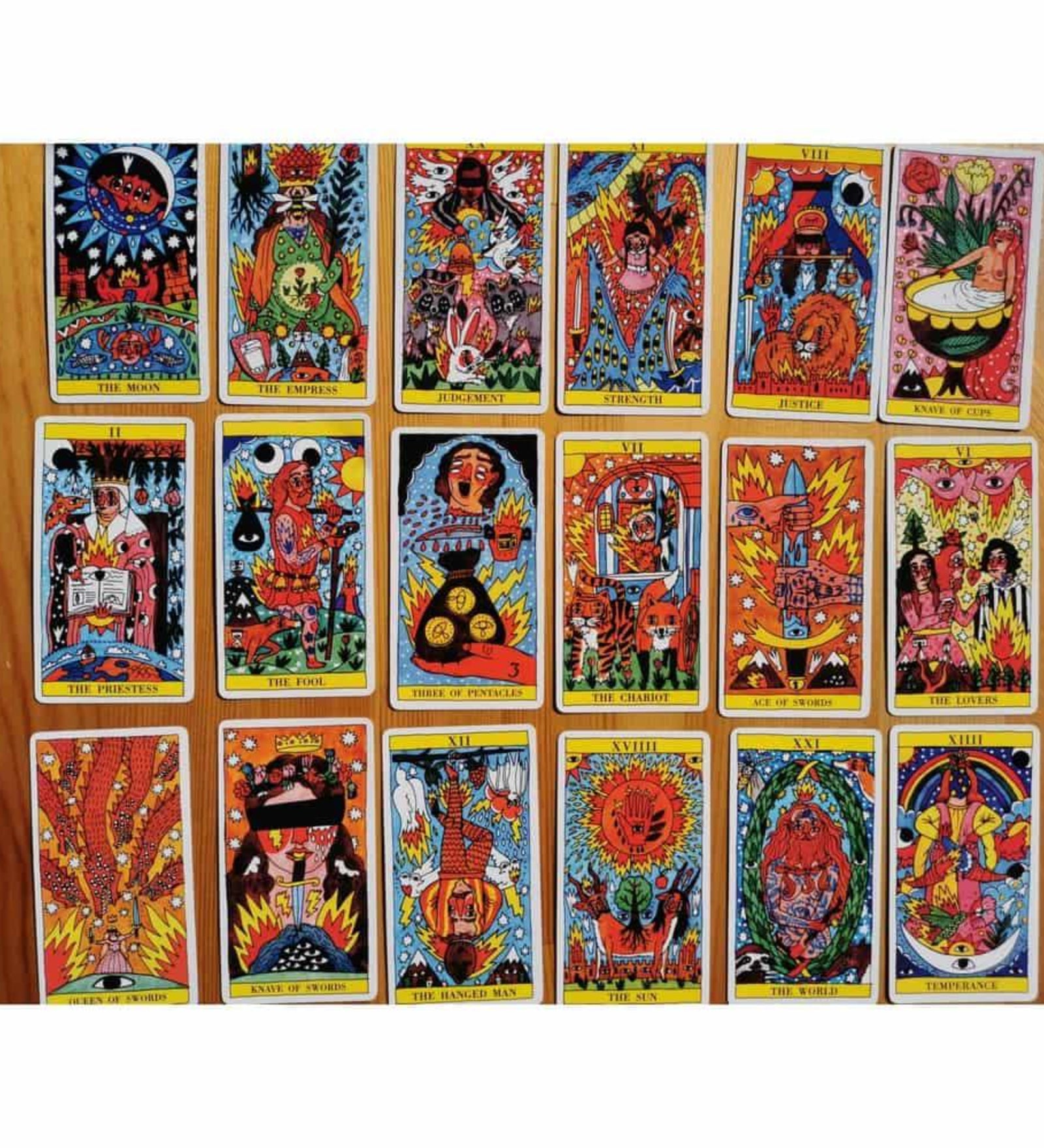 A képen a „Tarot del Fuego” kártyacsomag több lapja látható szétterítve, színes, kézzel rajzolt illusztrációkkal. Ricardo Cavolo stílusában készült grafikák vibráló színekben pompáznak: élénk vörös, sárga, narancs és kék tónusok dominálnak. A kártyákon mitikus és spirituális jelenetek jelennek meg, tűzmotívumokkal, szemekkel, szívekkel, napokkal és csillagokkal díszítve. A kártyák angol nyelvű felirattal vannak ellátva, pl. The Moon, The Fool, The Lovers.