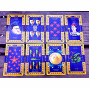 A képen a Frida Kahlo Tarot kártyacsomag egy válogatott lapjai láthatók, színes és gazdagon díszített dizájnnal. A kártyák domináns színe a mélykék és arany, amelyet virágminták és mexikói népművészeti motívumok egészítenek ki. Több kártyán is megjelenik Frida Kahlo portréja, különböző szimbólumokkal kiegészítve. A „The Magician” és „The Moon” lapokon a festőnő ikonikus arcképe szerepel, míg más lapokon paprikák, virágok, aranyérmék és festmények utalnak Frida életére és művészetére. 