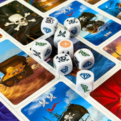 Tengeri Veszedelem társasjáték egyedi dobókockái és kártyái közelről, kard, koponya, gyémánt és kalóz szimbólumokkal kirakott játéktéren.