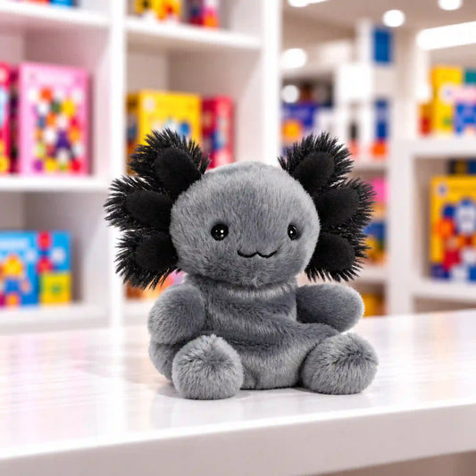 Mosolygós fekete axolotl plüssfigura, fekete, bolyhos külső kopoltyúkkal és puha tapintású kialakítással, játékbolti környezetben.