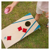 Felülnézetből látható, ahogy egy gyermek piros és csíkos zsákokat dob a BS Toys Cornhole Set kék mintás táblájára.